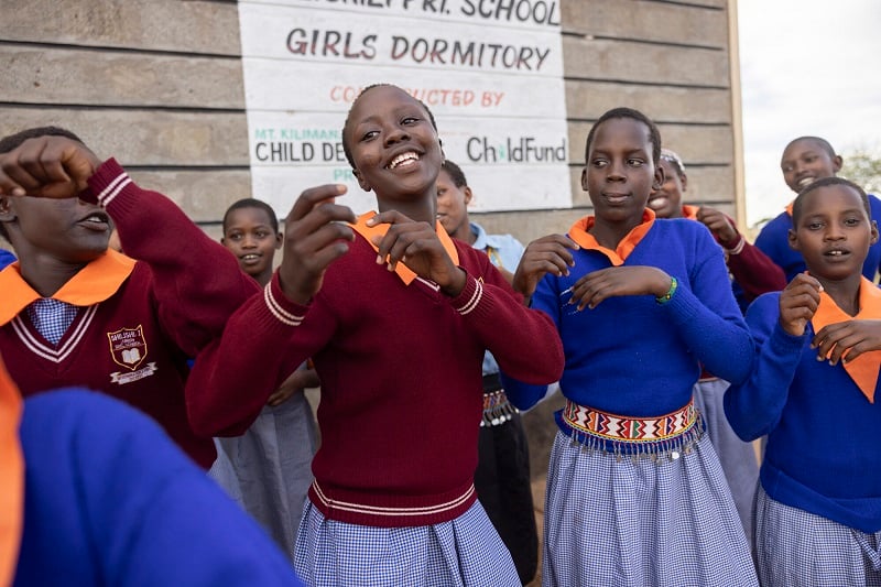 A teenage girl in Kenya dances with a group of other girls.