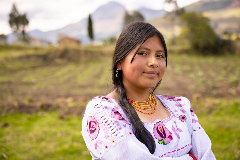 A teen girl in Ecuador looks somberly at the camera with folded arms, slightly smiling.