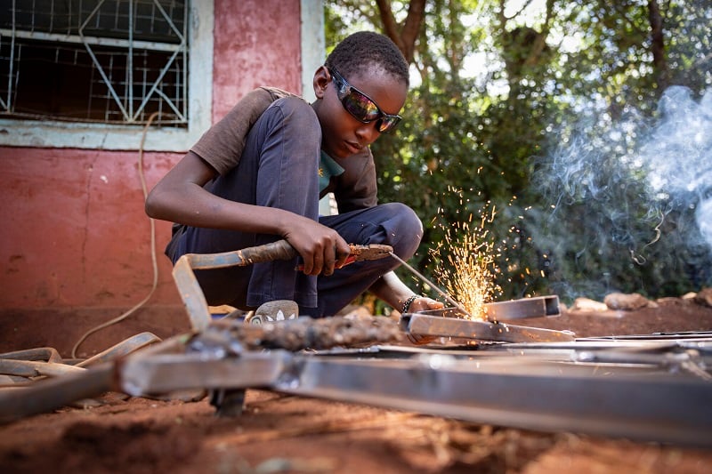 A teen boy in Kenya makes sparks fly as he welds, goggles on.
