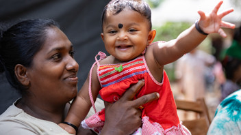 Held by her mother, a baby in Sri Lanka smiles and reaches out an arm to wave.