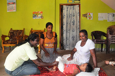 Anoma, a volunteer with one of ChildFund's local partners in Sri Lanka, does exercises with Umesha while her mother and grandmother look on.