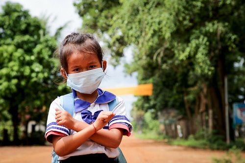 Girl in Cambodia stands looking at camera wearing mask