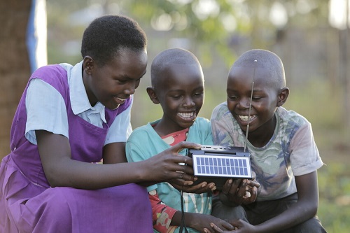 Girl and her siblings in Kenya sit around a radio, smiling